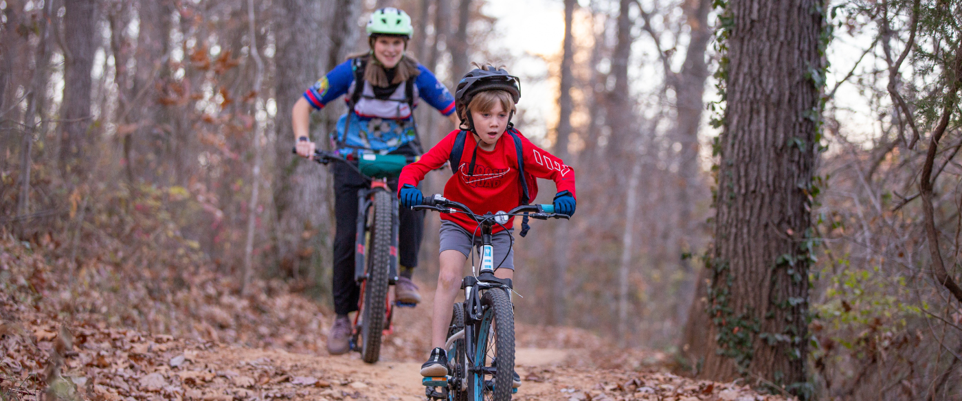 Pedal Kids coach riding with boy on mountain bike in a group class