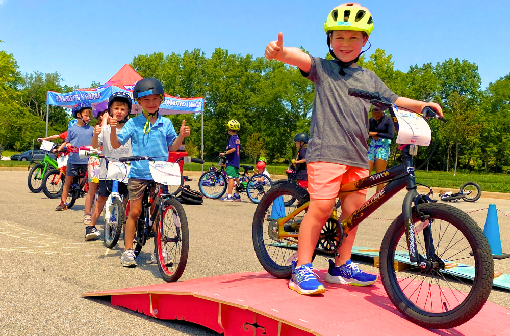 Child in learn to pedal bicycle class with thumbs up excited
