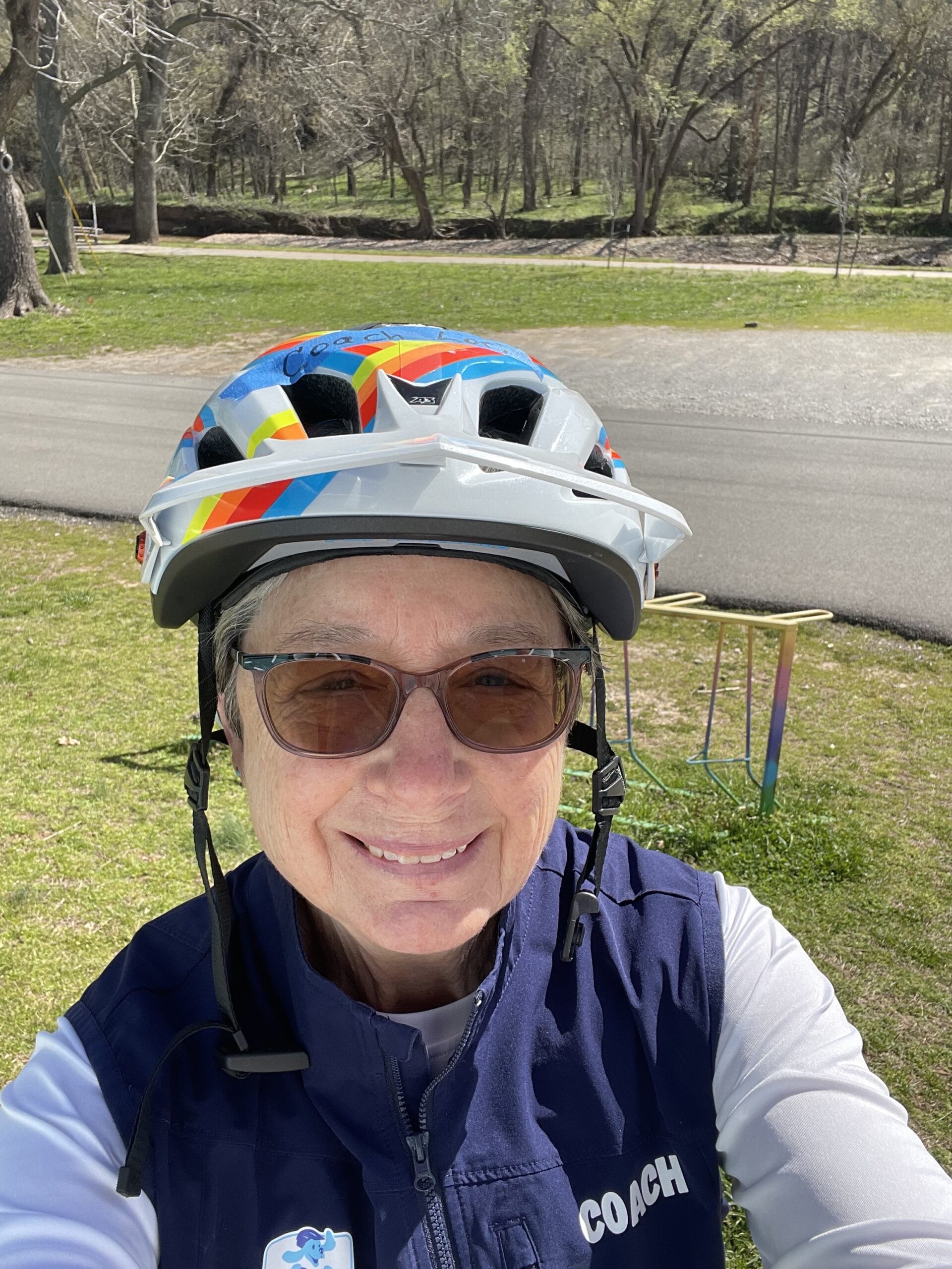 Coach Lori smiling outdoors in her colorful bike helmet and coach vest