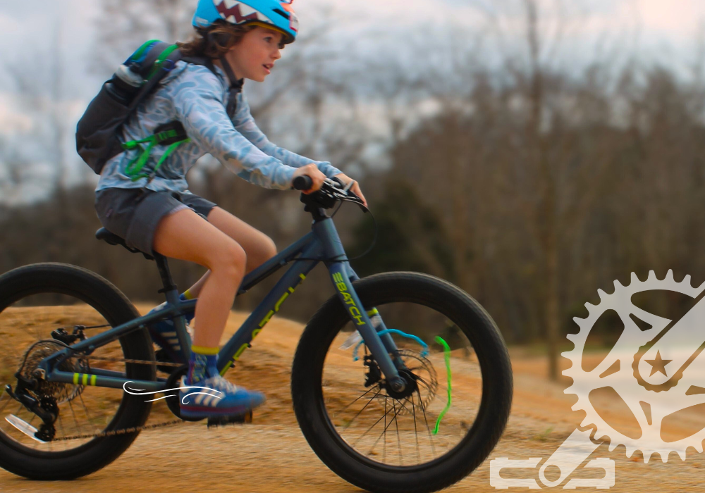 A child wearing a helmet and backpack rides a mountain bike on a dirt trail during spring break bike camp.